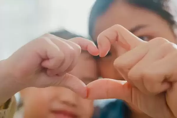 Closeup of young foster child making fingers heart shaped signs with foster mom