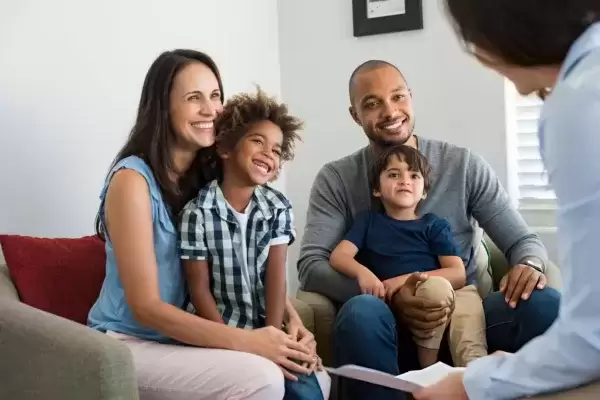Foster mom sitting with foster child on chair next to foster dad sitting in a chair with foster son 