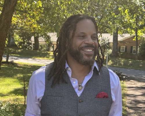 Wil Brown in a white shirt with a gray waste cote in a park