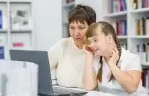 A Down syndrome girl with a foster mother looking at a laptop
