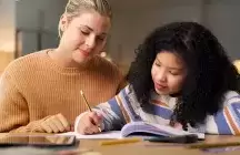 A foster mom helping a foster girl child with homework at a desk