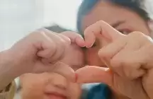 closeup of young foster child making fingers heart shaped sings with foster mom