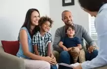 Foster mom sitting with foster child on chair next to foster dad sitting in a chair with foster son 