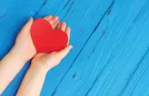 Kids hands holding a red heart on a blue background