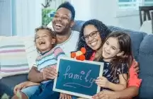 Happy foster to adopt family sitting on a couch holding a family sign 