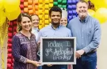 Teenagers holding a sign with his foster to adopt parents of his adoption date