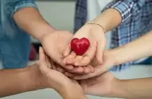 foster parents hands holding a little red heart