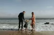 Two foster parents by seaside with a small child playing in the waves