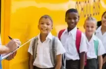 School kids lining up next to a bus to get on.