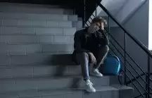 Teen boy sitting on dark stairs with backpack by his side