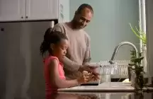 Foster father helping foster daughter wash her hands in the kitchen 