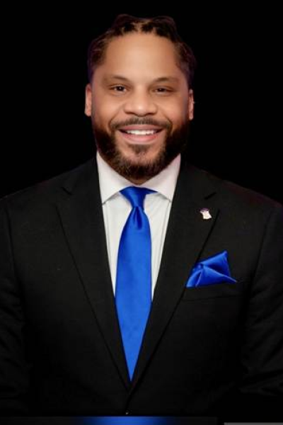 Wil Brown in a black suit with a blue tie with a black background